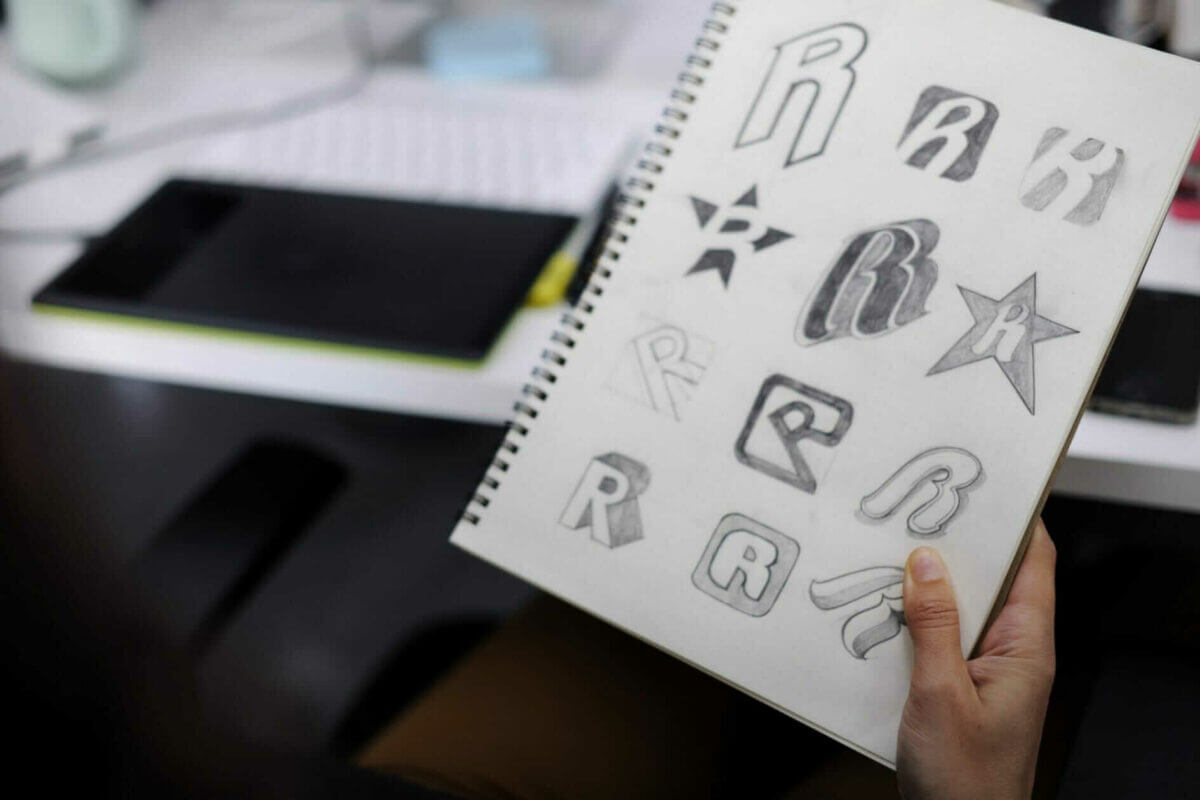 Our logo design expert Hand Holding Notebook With sketches of logos.