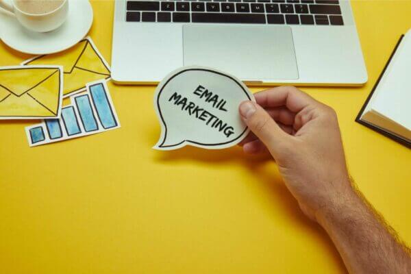 email-marketing-service-cropped-image-of-man-holding-speech-bubble-with-email-marketing-lettering-near-laptop