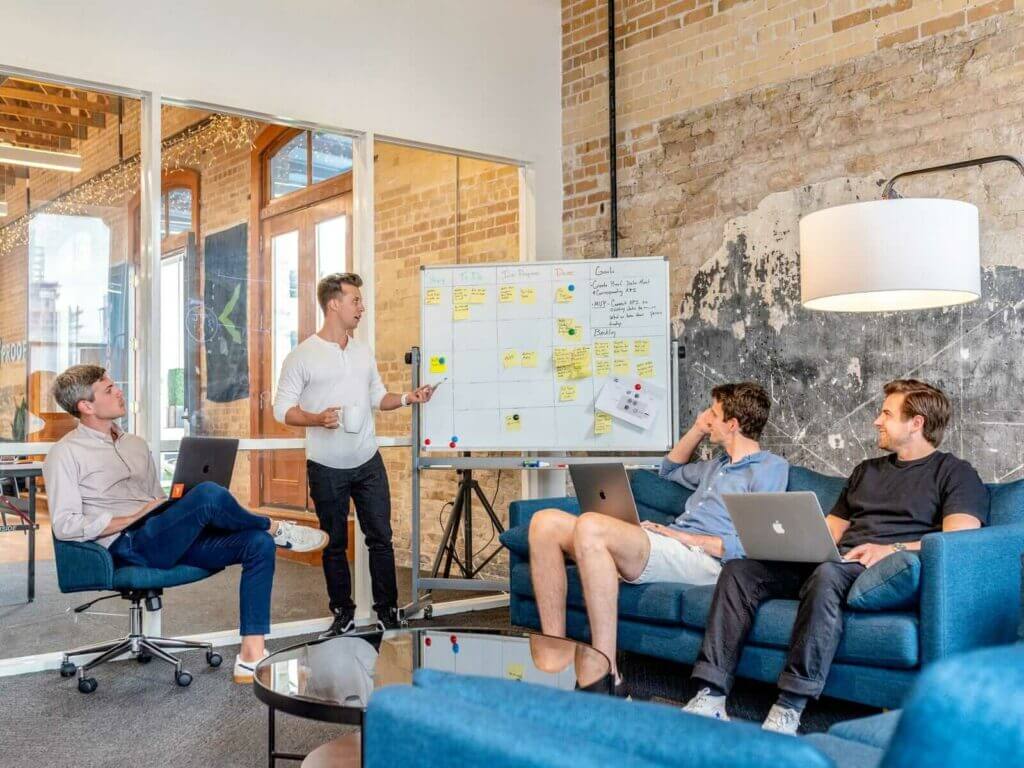 estate-agent-web-design-team-three men sitting while using laptops and watching man beside whiteboard