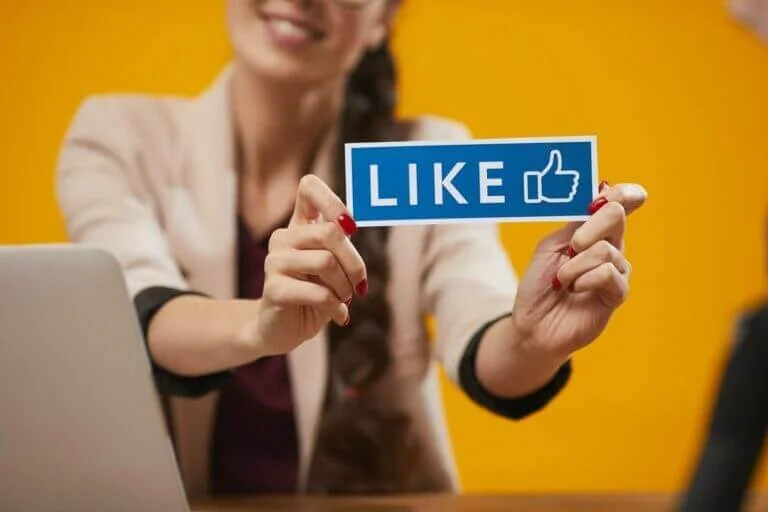 a woman holding up a facebook like sign for social media marketing report of interactions.