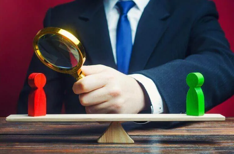 a man with a magnifying glass looking at a red wooden person shape for social media marketing competitors.